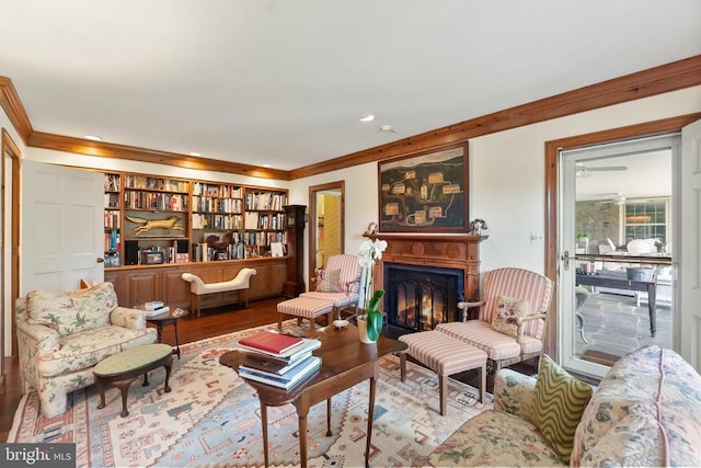 living area with crown molding, wood finished floors, a glass covered fireplace, and recessed lighting