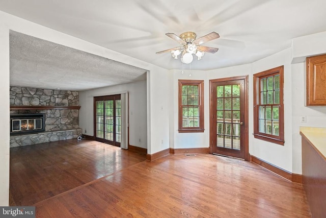  - unfurnished living room with wood finished floors, ceiling fan, and a stone fireplace