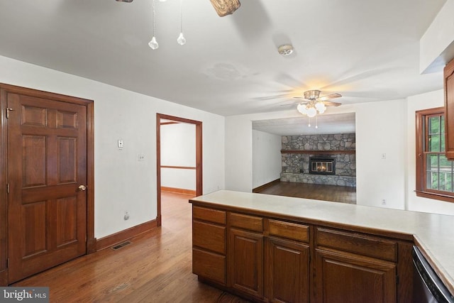  - kitchen featuring ceiling fan, dark wood finished floors, light countertops, and a stone fireplace