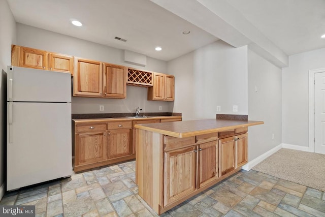 kitchen featuring freestanding refrigerator, a sink, light stone finish flooring, recessed lighting, and a peninsula