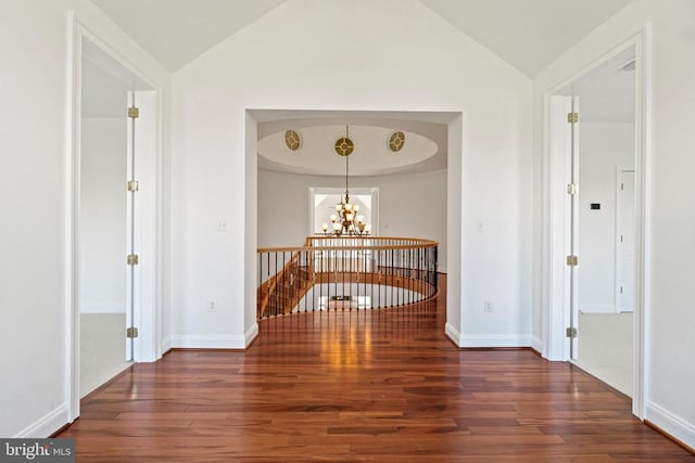 hallway featuring wood finished floors, a chandelier, vaulted ceiling, an upstairs landing, and baseboards