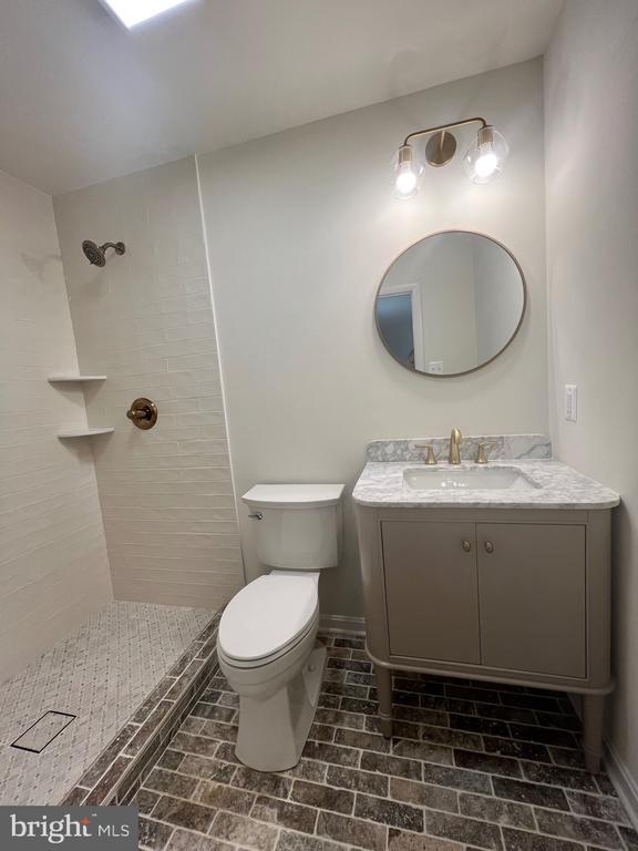 377 Cleveland St, Warrenton, VA 20186 - bathroom featuring a tile shower, toilet, brick patterned floors, vanity, and baseboards