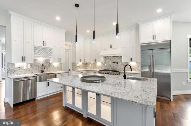 kitchen with premium range hood, white cabinetry, a center island with sink, appliances with stainless steel finishes, and pendant lighting