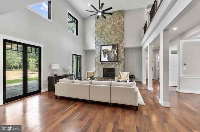 living room featuring ceiling fan, dark hardwood / wood-style floors, and a stone fireplace