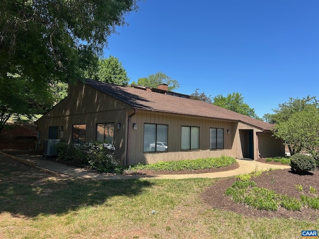 rear view of property with central air condition unit, a chimney, and a lawn