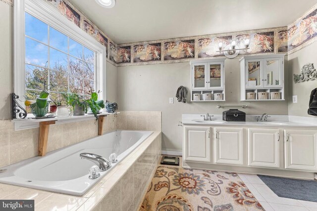 bathroom with a relaxing tiled tub, vanity, and tile patterned flooring