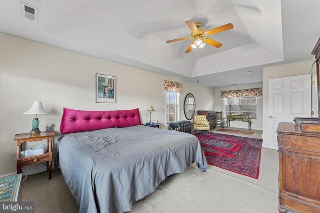 bedroom with light carpet, a raised ceiling, and ceiling fan