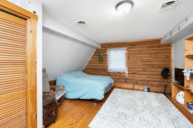 bedroom featuring wood-type flooring, rustic walls, and visible vents