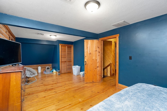 bedroom featuring light wood finished floors, a textured ceiling, and visible vents