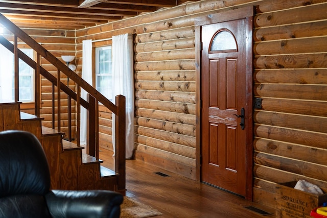 entrance foyer with log walls, wood finished floors, visible vents, and stairs