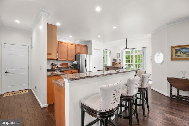  - kitchen with freestanding refrigerator, a kitchen island with sink, dark wood-type flooring, ornamental molding, and a kitchen breakfast bar