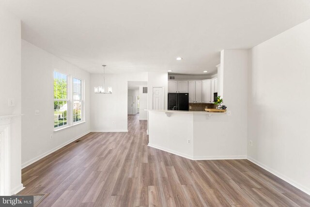  - unfurnished living room with a chandelier, light wood-style floors, recessed lighting, and baseboards