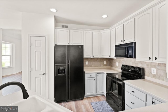  - kitchen featuring black appliances, white cabinetry, light wood finished floors, backsplash, and light countertops