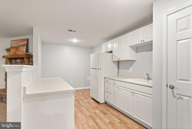  - kitchen with a sink, freestanding refrigerator, light countertops, light wood-style flooring, and white cabinetry