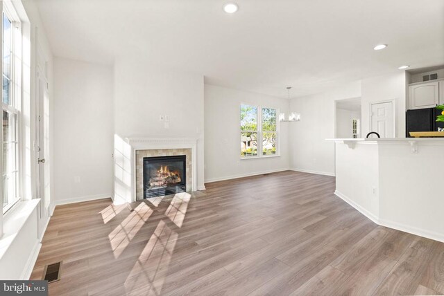  - unfurnished living room featuring a tile fireplace, a chandelier, light wood-style flooring, recessed lighting, and baseboards