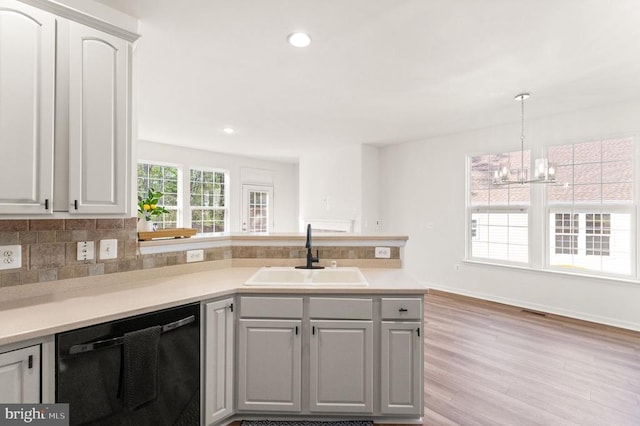  - kitchen featuring dishwashing machine, a sink, a peninsula, a chandelier, and light countertops