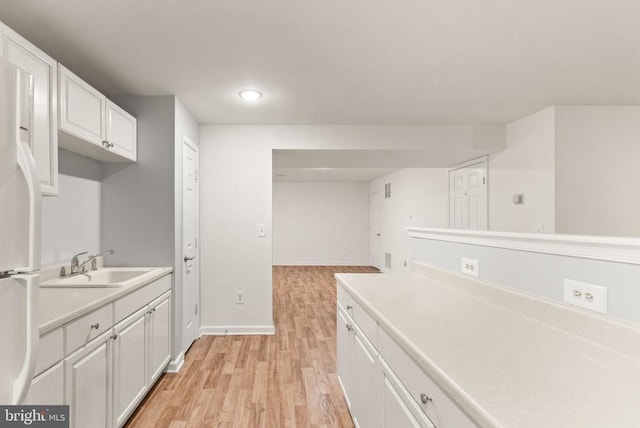  - kitchen featuring light wood-style flooring, light countertops, white cabinetry, a sink, and white fridge
