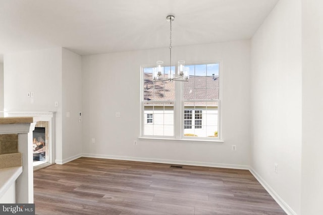  - unfurnished dining area featuring a chandelier, wood finished floors, a glass covered fireplace, and baseboards