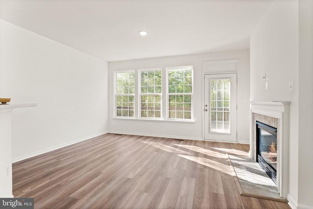  - unfurnished living room featuring a glass covered fireplace, healthy amount of natural light, wood finished floors, baseboards, and recessed lighting