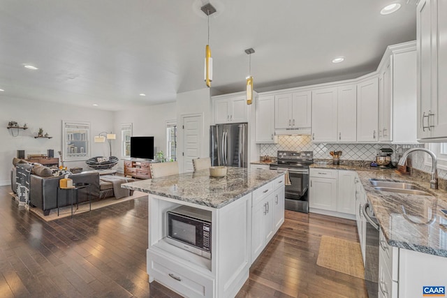 kitchen with a sink, under cabinet range hood, open floor plan, white cabinets, and appliances with stainless steel finishes