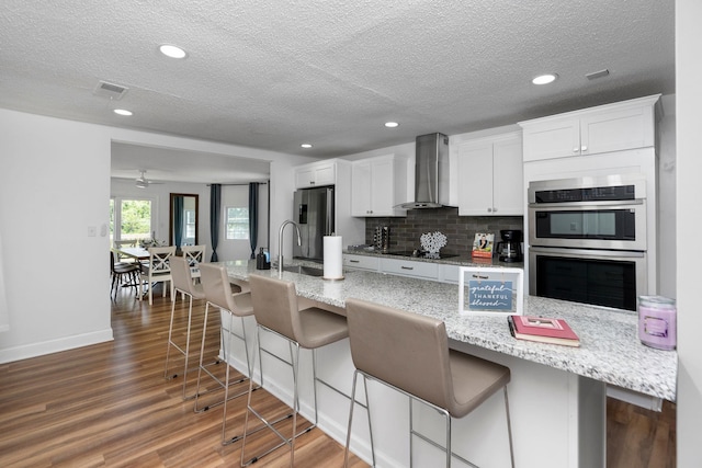 2003 Rinacas Corner Rd, Shenandoah, VA 22849 - kitchen featuring wall chimney exhaust hood, appliances with stainless steel finishes, a textured ceiling, a kitchen bar, and white cabinets