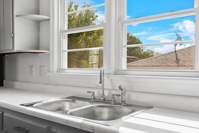 kitchen view of a sink, gray cabinets, open shelves, and light countertops