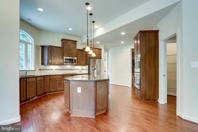 kitchen featuring stainless steel appliances, hardwood / wood-style flooring, backsplash, a center island, and stone countertops