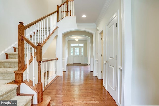 hallway featuring arched walkways, light wood-style flooring, stairway, ornamental molding, and recessed lighting