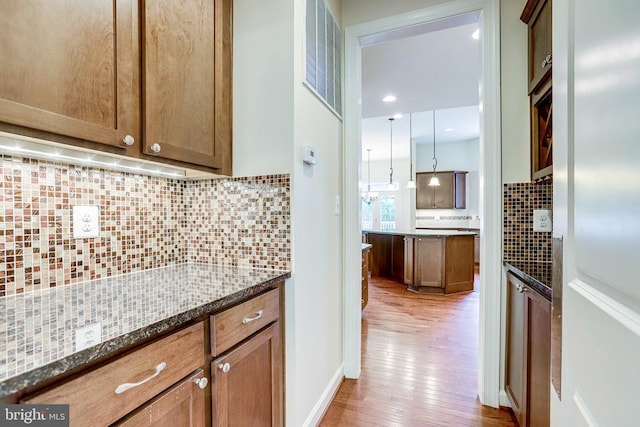 kitchen featuring light wood finished floors, tasteful backsplash, dark stone counters, and brown cabinets