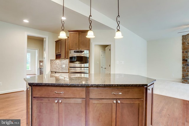 kitchen featuring stainless steel double oven, light wood finished floors, dark stone counters, hanging light fixtures, and baseboards