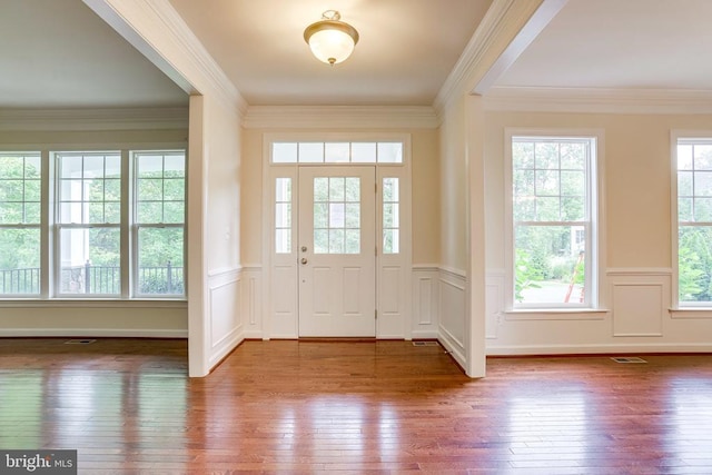entrance foyer with wood-type flooring, a wainscoted wall, crown molding, and a decorative wall