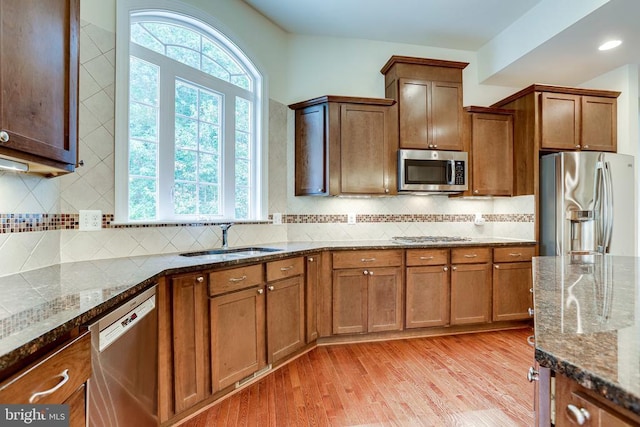 kitchen featuring stainless steel appliances, a sink, light wood-type flooring, dark stone countertops, and brown cabinetry