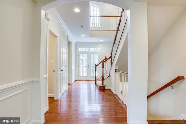 foyer entrance with ornamental molding, wood finished floors, french doors, stairs, and arched walkways