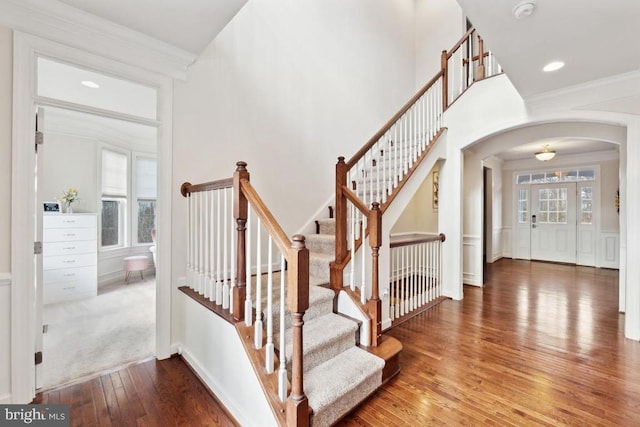 stairway featuring arched walkways, wood-type flooring, and crown molding