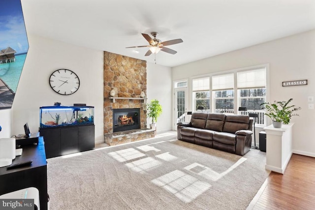 living room with ceiling fan, wood finished floors, a stone fireplace, and baseboards
