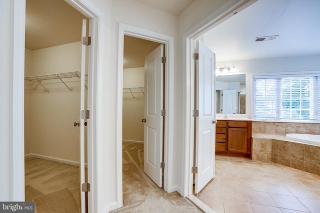 bathroom with vanity, tiled tub, a walk in closet, and tile patterned flooring