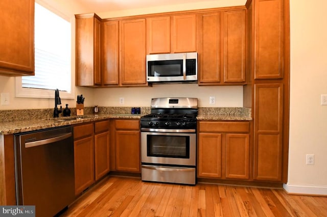 kitchen featuring brown cabinetry, appliances with stainless steel finishes, a sink, light stone counters, and light wood finished floors