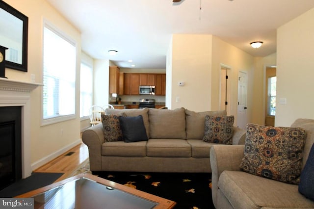 living room featuring baseboards, a ceiling fan, light wood-style flooring, and a glass covered fireplace