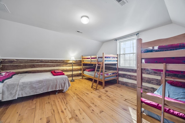 bedroom featuring lofted ceiling, wood-type flooring, visible vents, and wood walls