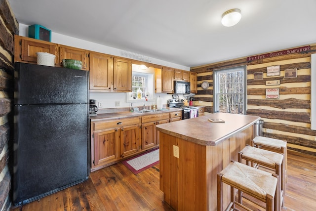 kitchen featuring a sink, a kitchen breakfast bar, a kitchen island, black appliances, and dark wood-style floors