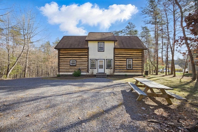rear view of house with roof with shingles, entry steps, and driveway