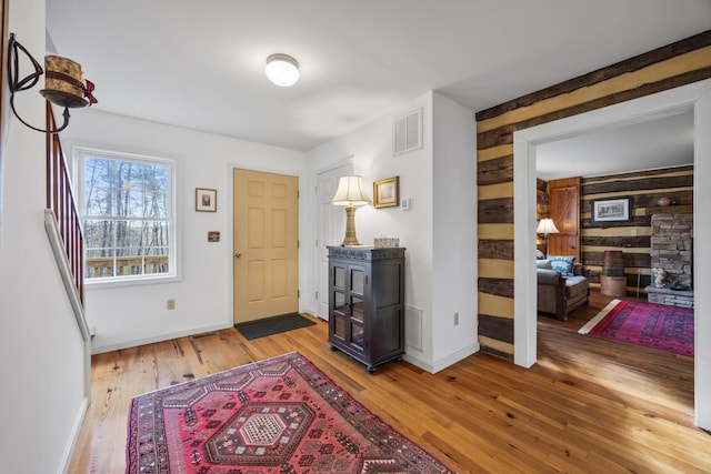 foyer entrance with light wood-type flooring, baseboards, wood walls, and visible vents