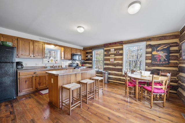 kitchen featuring a center island, a wealth of natural light, a kitchen bar, black appliances, and dark wood-style floors