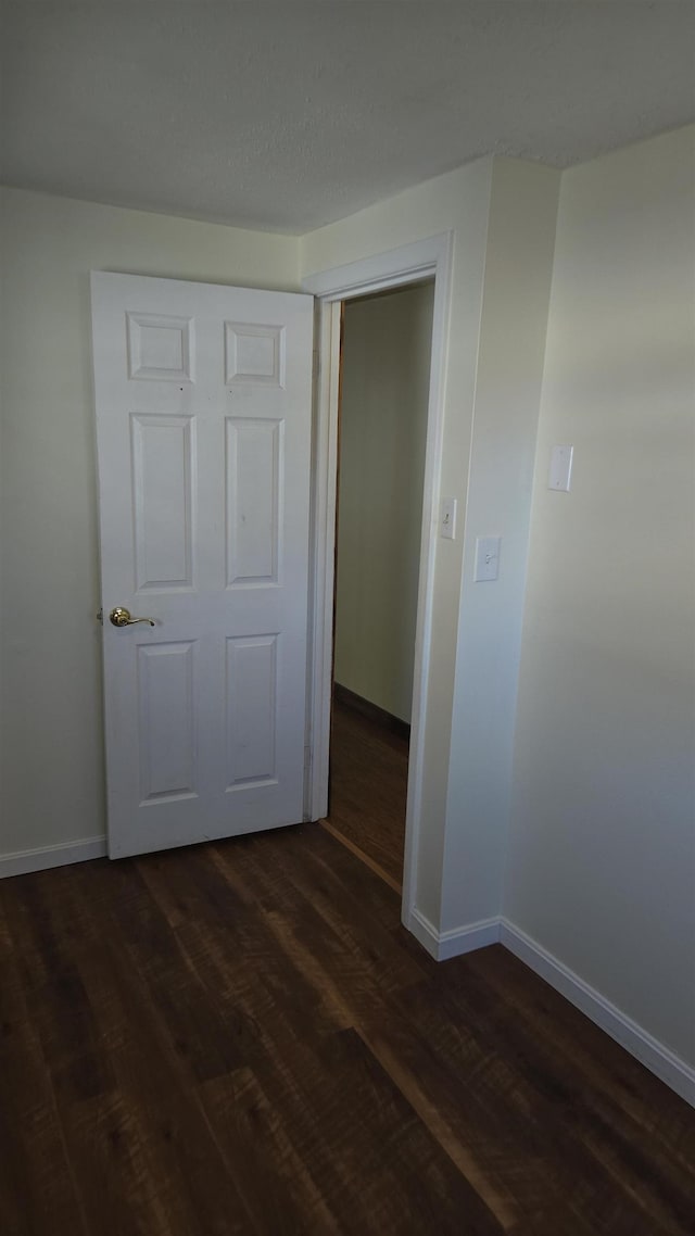 unfurnished bedroom with a closet, dark wood finished floors, and baseboards