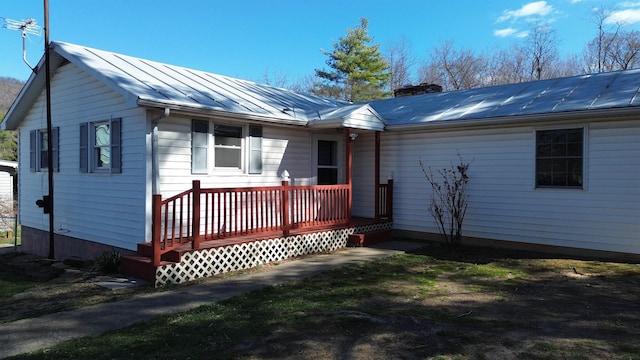 view of front facade with a chimney, metal roof, a standing seam roof, and a wooden deck