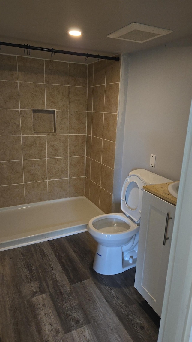 bathroom featuring a tile shower, vanity, toilet, and wood finished floors