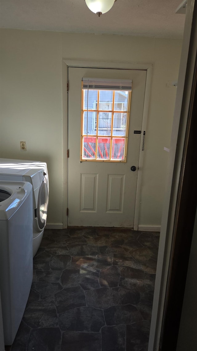 clothes washing area featuring washing machine and clothes dryer, laundry area, baseboards, and stone finish flooring