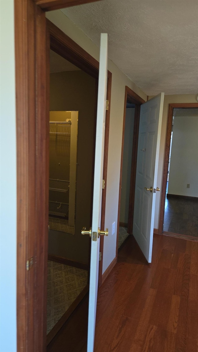 hallway with baseboards, a textured ceiling, and wood finished floors