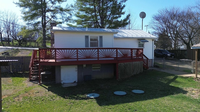rear view of property featuring metal roof, a deck, fence, and a lawn