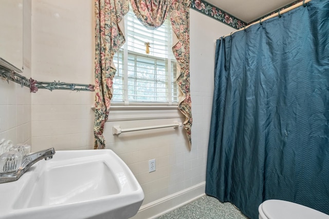 bathroom featuring a sink, tile walls, a wainscoted wall, toilet, and curtained shower